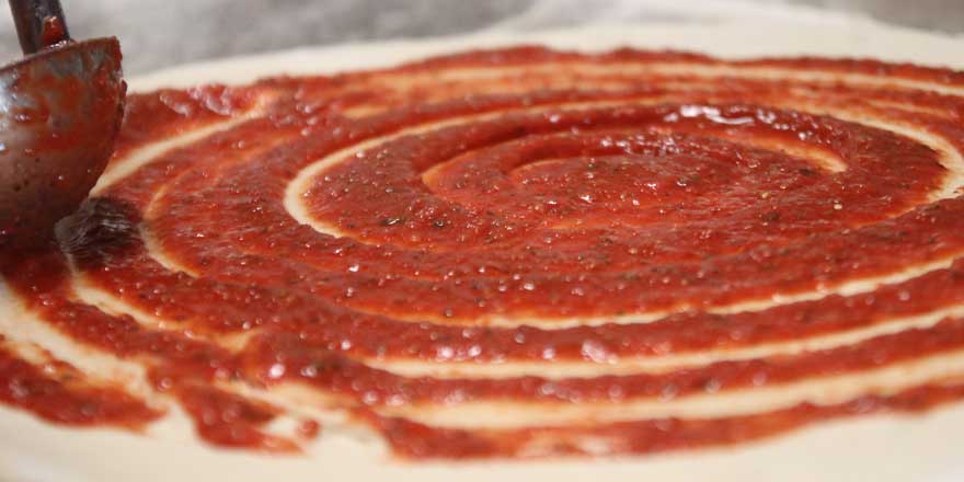 Photo of sauce being spread onto a pizza at GJP Italian Eatery in Oswego, NY.